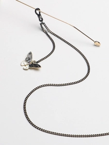 Macro detail of black metal eyeglass chain with enamel butterfly and gem embellishment