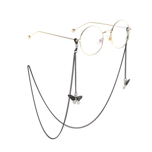 Golden round glasses with black chain and butterfly pendant charms on a white backdrop