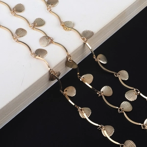 Elegant gold chain eyewear strap with textured shell pendants and wavy links on black surface