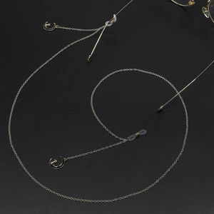 Gold eyeglasses chain with cat and moon pendants on a textured black background
