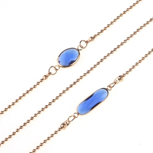 Détail de la chaîne de lunettes dorée avec cristaux bleus ovales sur fond blanc