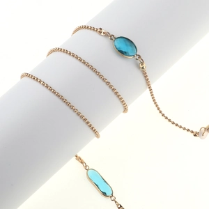 Chaîne à lunettes dorée avec perles et cristaux bleus sur un support blanc cylindrique