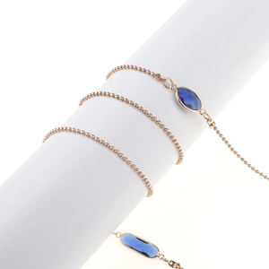 Chaîne de lunettes perlée dorée avec gemmes facettées bleues sur un support blanc