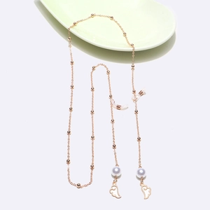 Détail d'une chaîne de lunettes dorée avec perles et breloques en forme d'ailes d'ange