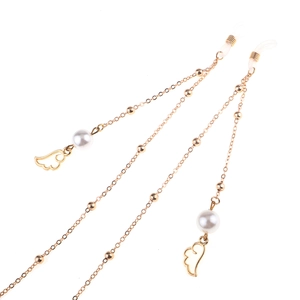 Chaîne à lunettes dorée avec perles blanches et pendentifs ailes sur fond blanc épuré