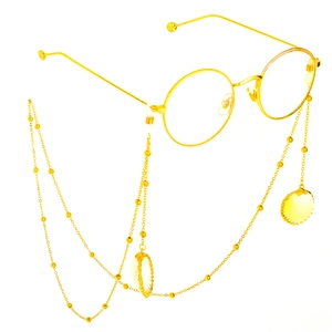 Golden round glasses frame with beaded shell chain and metal pendants on white background