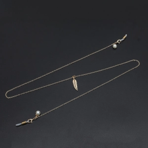 Golden metal glasses chain with leaf pendant and white pearl beads on black background