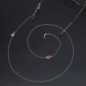 Goldene Brillenkette mit rosa Tropfen-Edelsteinen und Silikonschlaufen auf schwarzem Grund
