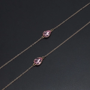 Goldene Brillenkette mit rosa Tropfenanhängern auf schwarzem texturiertem Hintergrund