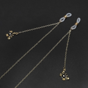 Golden eyewear chain with black crab pendants and white zircon accents on dark background