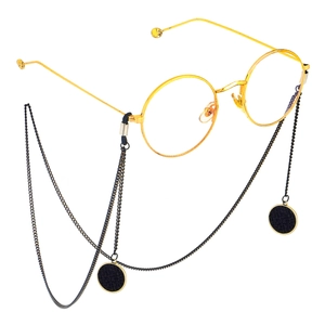 Lunettes rondes dorées avec chaîne en métal noir et pendentif tressé sur fond blanc