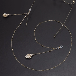 Gold metal eyewear chain with natural shell charms and delicate beads on dark background