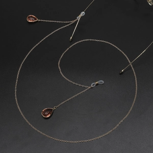 Golden metal glasses chain with amber teardrop pendants on a matte black background