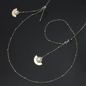 Chaîne de lunettes dorée avec perles blanches et breloques en métal sur fond noir