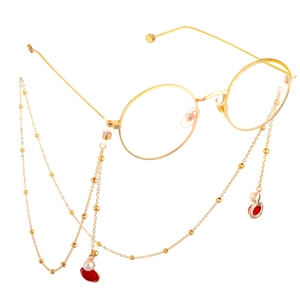 Chaîne de lunettes dorée avec perles blanches et pendentifs rouges sur lunettes rondes