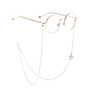Close-up of gold round glasses frame with a silver chain and white floral pendant