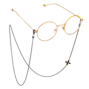 Close-up of golden round glasses with a black clover metal chain on white background
