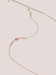 Close-up of golden glasses chain featuring pink faceted gemstone and matte gold beads