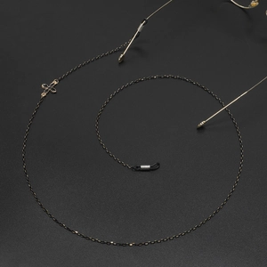 Fashionable black and gold metal eyewear chain with floral charms on matte background