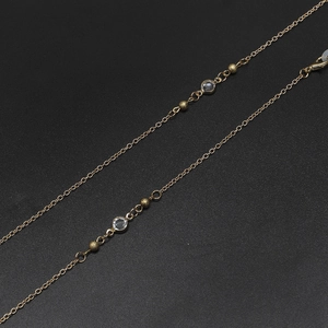 Detail of golden eyeglass chain with clear crystal beads and lobster clasp on black surface