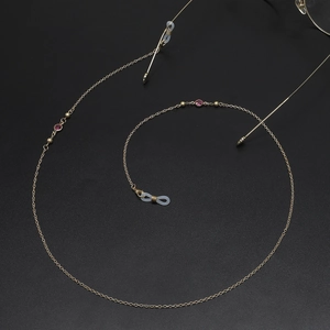 Handmade 70cm gold copper eyeglass chain with red glass beads on a black background