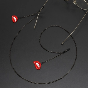Fashionable gold-rimmed glasses with black metal chain and red lip charms on dark surface