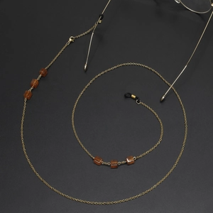 Goldene Brillenkette mit Bernsteinperlen und Silikonschlaufen auf schwarzem Grund