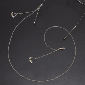 Macro detail of golden metal eyeglass chain with triangular pearl pendants on black background