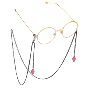 Lunettes rondes dorées avec chaîne en métal noir et breloques ballon rouge sur fond blanc