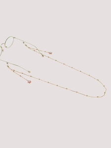 Détail de la chaîne de lunettes dorée avec pendentifs fleurs roses et perles blanches