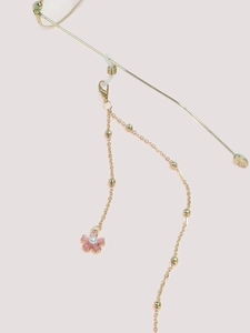Détail d'une chaîne de lunettes dorée avec pendentif fleur rose et perle nacrée