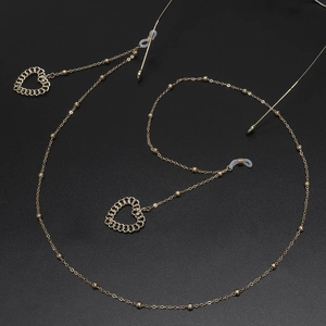 Chaîne de lunettes dorée avec pendentifs cœur et perles sur fond noir élégant