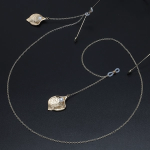 Golden eyeglass chain with leaf pendants and faux pearls on a black textured background
