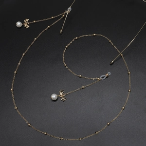 Goldene Brillenlkette mit Metallschleife und weißen Perlen auf schwarzem Grund