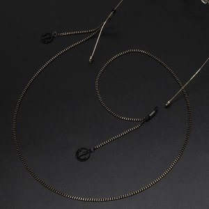 Gold metal eyewear chain with black anchor pendants and silicone connectors on black surface