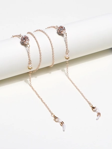 Rose gold glasses chain with rhinestones and pearls on a minimalist white stand