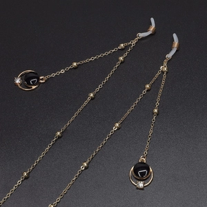 Elegant gold eyeglass chain with black rhinestone pendant and pearl beads on dark background