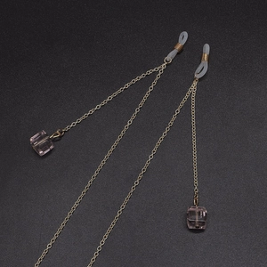 Golden chain eyeglass strap with pink crystal cube charms on a dark textured surface