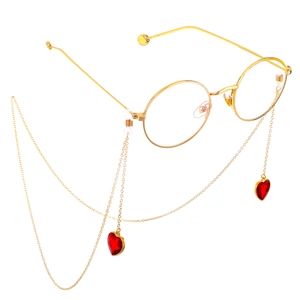 Detail van de gouden brillenketting met rode hartkristallen aan een ronde bril