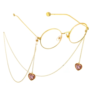 Detail van gouden brillenketting met roze hartvormige kristallen hangers en montuur