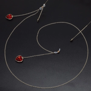 Detailopname van gouden brillenketting met rode hartvormige kristallen op een zwarte