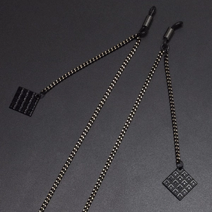 Fashionable black eyewear chain with square pendant and gold accents on textured surface