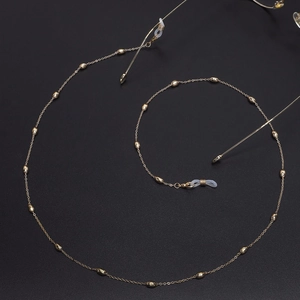 Elegant gold oval bead glasses chain in a spiral layout on black textured surface