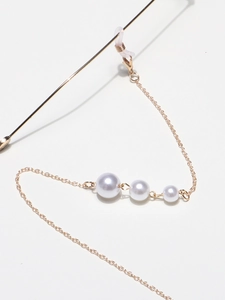 Detail of elegant gold eyewear chain featuring triple white pearls and lobster clasps
