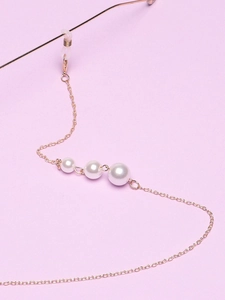 Close-up of golden glasses chain with three white pearls on a light purple background
