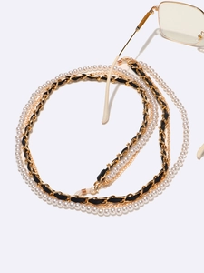 Detail of layered eyewear chain with white pearls and gold metal black ribbon links