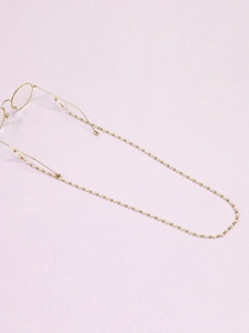 Vue détaillée du cordon de lunettes doré avec petites perles blanches sur fond mauve