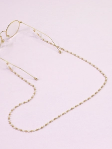 Détail d'une chaîne de lunettes avec billes dorées et perles blanches sur lavande