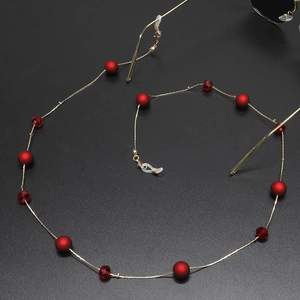 Goldene Brillenlkette mit roten matten Perlen und Kristallen auf schwarzem Hintergrund