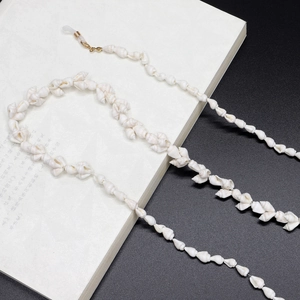 Minimalist white conch shell eyewear chain with golden clasps on a white book